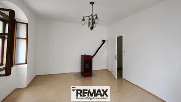 Helles Zimmer mit Holzparkettboden und einem modernen Holzofen als Wärmequelle.