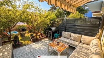 Gemütliche Terrasse mit Markise, Sitzgelegenheiten und Grillbereich im Garten.