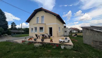 Helles Einfamilienhaus mit Holzterrasse und Gartenbereich unter blauem Himmel.