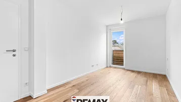 Helles, leeres Zimmer mit Holzparkett und Zugang zu einem französischen Balkon oder einer kleinen Terrasse.