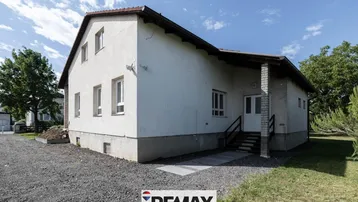 Einfamilienhaus mit heller Fassade und Kiesauffahrt unter blauem Himmel.