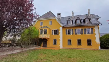 Rückseite des historischen Gebäudes mit gelber Fassade, Gaubenfenstern und weitläufigem Gartenbereich mit Bäumen.