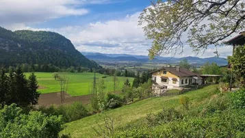 Haus in idyllischer ländlicher Umgebung mit weitem Blick auf grüne Hügel und Berge.