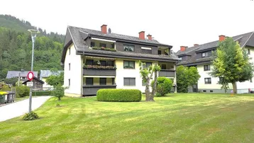 Mehrfamilienhaus mit gepflegter Grünfläche und Bergblick in ländlicher Umgebung.