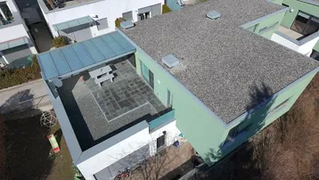 Luftaufnahme eines modernen Hauses mit großer, überdachter Terrasse und angrenzendem Gartenbereich.