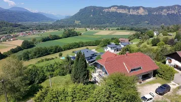 Panoramablick auf ein Haus mit rotem Dach, umgeben von grünen Hügeln und einem weiten Tal.