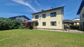Großzügiger Gartenbereich mit Rasenfläche und Blick auf das Haus unter blauem Himmel.