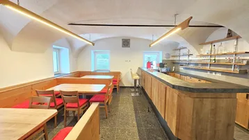 Einladender Gastraum mit Holztischen, gepolsterten Bänken und einer gut ausgestatteten Bar.