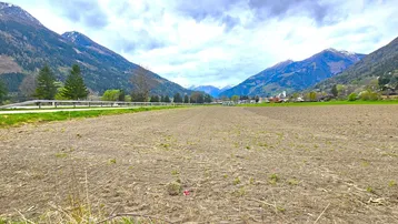 Weitläufiges Ackerland mit Blick auf die umliegende Berglandschaft und ein kleines Dorf in der Ferne.