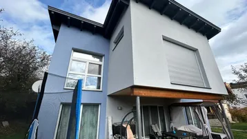 Modernes Haus mit blauer und grauer Fassade, davor eine möblierte Terrasse und Trampolin.