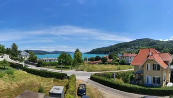 Panoramablick auf den See mit umliegenden Häusern und grünen Hügeln unter blauem Himmel.