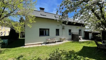 Hinteransicht des Hauses mit gepflegtem Garten und blühenden Bäumen unter blauem Himmel.