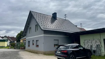 Ansicht des Einfamilienhauses mit Satteldach und einem geparkten Auto auf dem Kiesparkplatz.