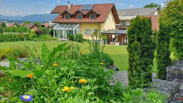 Gepflegter Garten mit blühenden Pflanzen, Rasenfläche und Blick auf das Haus mit Wintergarten.