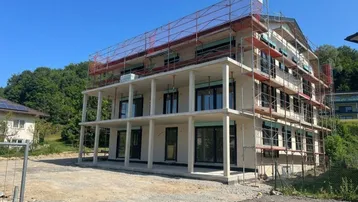 Neubau im Bau mit Gerüst und Blick auf die Umgebung unter blauem Himmel.