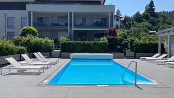 Moderner Außenbereich mit Schwimmbad, Liegestühlen und gepflegter Gartenanlage vor dem Gebäude.