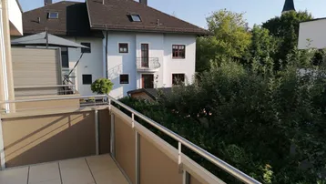 Blick von einem Balkon mit Fliesenboden auf ein benachbartes Haus und einen Kirchturm.