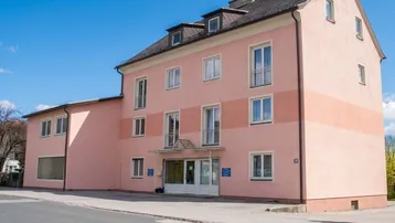 Rosa gestrichenes Mehrfamilienhaus mit mehreren Etagen und Dachgauben unter blauem Himmel.