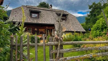 Traditionelles Holzhaus mit Schindeldach und rustikalem Zaun in alpiner Landschaft.