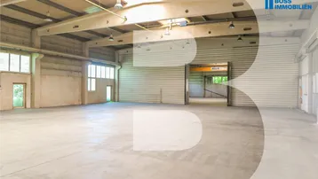 Geräumige, leere Lagerhalle mit hohen Decken, Betonboden und großen Fenstern, die viel Tageslicht hereinlassen.