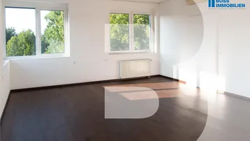 Heller Büroraum mit dunklem Holzboden und großen Fenstern, die viel Tageslicht hereinlassen.
