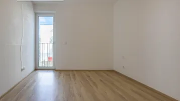 Helles Schlafzimmer mit Laminatboden und Zugang zu einem französischen Balkon.
