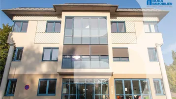 Modernes Bürogebäude mit großen Fenstern und blauen Rahmen unter klarem Himmel.