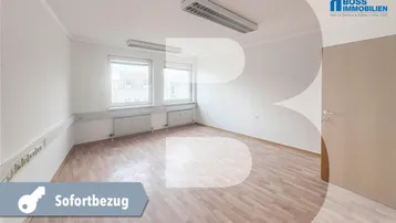 Helles, leeres Büro mit Holzfußboden und großen Fenstern, bereit für den sofortigen Bezug.