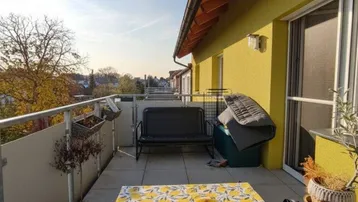 Sonniger Balkon mit Esstisch, Sitzbank und weitem Blick über die Dächer.