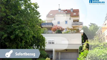 Mehrfamilienhaus mit mehreren Balkonen und integrierter Tiefgarage, umgeben von viel Grün.