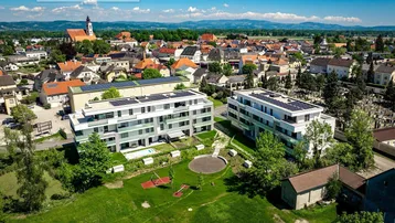 Luftaufnahme einer modernen Wohnanlage mit Grünflächen, Spielplatz und Gemeinschaftspool in ländlicher Umgebung.