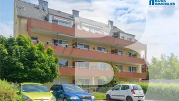 Mehrstöckiges Apartmentgebäude mit Balkonen und Parkplätzen im Freien unter blauem Himmel.
