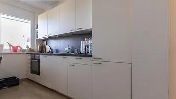 Helle Küche mit weißen Schränken, dunkler Arbeitsplatte und integriertem Backofen.