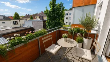 Gemütlicher Balkon mit Sitzgelegenheiten, Blumenkästen und Blick auf die umliegenden Gebäude.