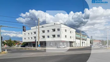 Modernes Mehrfamilienhaus mit weißer Fassade, Balkonen und Geschäftsflächen an einer Straßenecke.