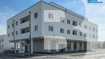 Modernes, weißes Mehrfamilienhaus mit klaren Linien, Balkonen und Geschäftsflächen im Erdgeschoss an einer Straße.