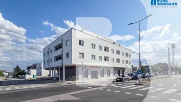 Modernes weißes Mehrfamilienhaus an einer Straßenecke mit Geschäften im Erdgeschoss und Balkonen.