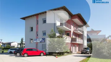 Modernes Mehrfamilienhaus mit mehreren Balkonen und Parkplätzen im Freien unter blauem Himmel.