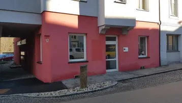 Gebäudefassade mit markanter rosa-roter Farbgebung und Eingangsbereich an einer ruhigen Straße.