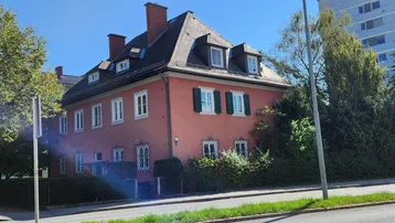 Traditionelles Gebäude mit roter Fassade, grünen Fensterläden und Dachgauben unter blauem Himmel.