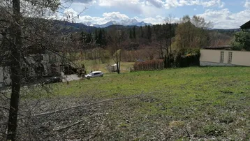 Grünes Grundstück mit weitem Blick auf eine Bergkette, Bäume und einige Gebäude in der Landschaft.