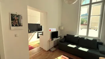 Helles Wohnzimmer mit Holzboden, Sofa und offenem Zugang zu einer modernen Küche.