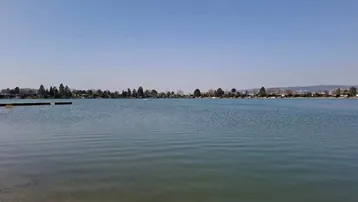 Weitläufiger Blick über einen ruhigen See mit bewaldetem Ufer und klarem Himmel.