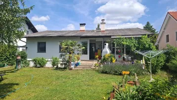 Blick auf das Haus von hinten mit einem gepflegten Garten und einer überdachten Terrasse.
