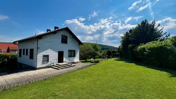 Weißes Einfamilienhaus mit großem, gepflegten Rasen und Blick auf die umliegende Hügellandschaft.