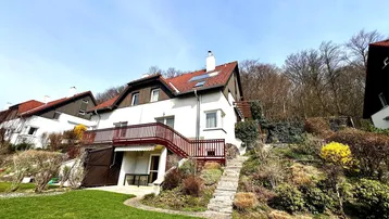 Weißes Einfamilienhaus mit rotem Dach, umgeben von einem terrassierten Garten und Bäumen.
