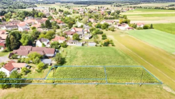 Luftaufnahme eines Grundstücks mit blauer Markierung, umgeben von grünen Feldern und einem Dorf im Hintergrund.