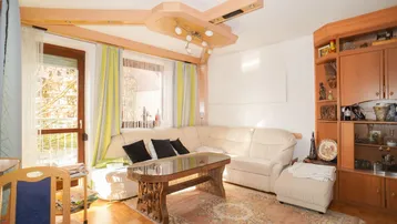 Helles Wohnzimmer mit beigem Sofa, Holzbalken an der Decke und Zugang zum Balkon.