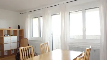 Heller Essbereich mit Holztisch, Stühlen und Zugang zum Balkon durch große Fenster.