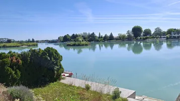 Weitläufiger Blick auf einen ruhigen See mit grünen Ufern und klarem, blauem Himmel.